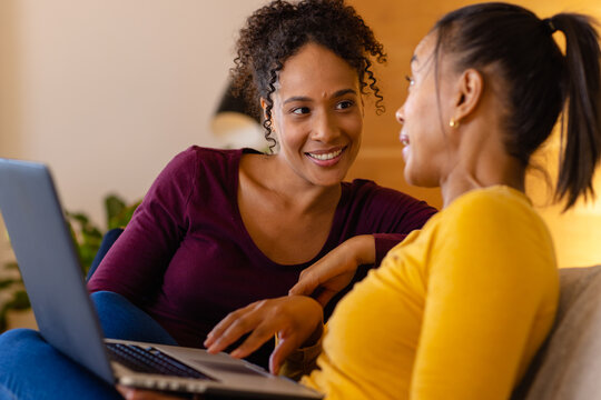 Happy biracial lesbian couple using laptop on sofa in living room