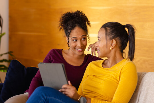 Happy biracial lesbian couple using tablet on sofa in living room