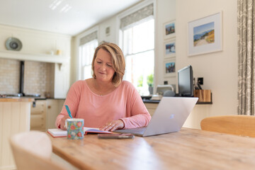 Woman using laptop working from home in kitchen
