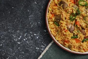 Delicious pilaf with meat on black textured table, top view. Space for text