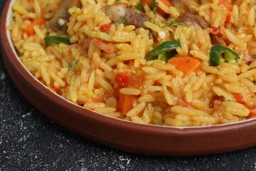 Delicious pilaf with meat on black textured table, closeup