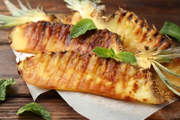 Tasty grilled pineapple pieces and mint leaves on wooden table, closeup