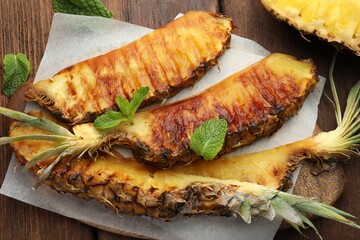 Tasty grilled pineapple pieces and mint leaves on wooden table, flat lay