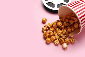 Bucket with tasty popcorn and film reel on pink background