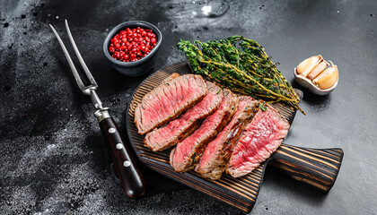 Sliced grilled roast beef with fork for meat on wooden cutting board. Black background. Top view.