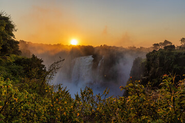 Wide panorama of victoria falls at sunset with orange sun in the sky
