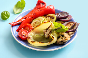 Plate with tasty grilled vegetables on blue background