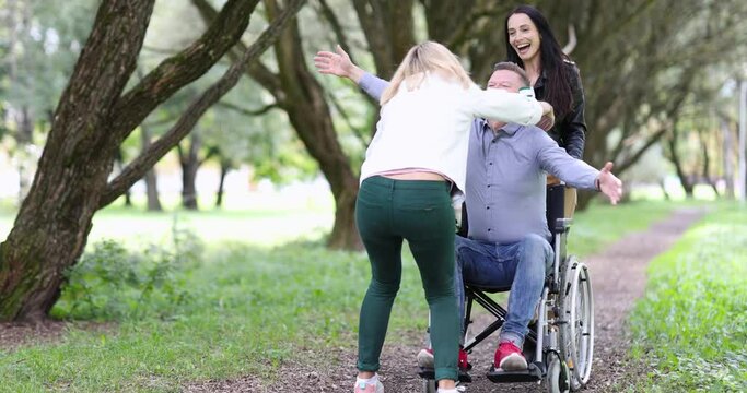 Young woman hugs happy man in a wheelchair on walk in park 4k movie. Friends psychological support for disabled people concept