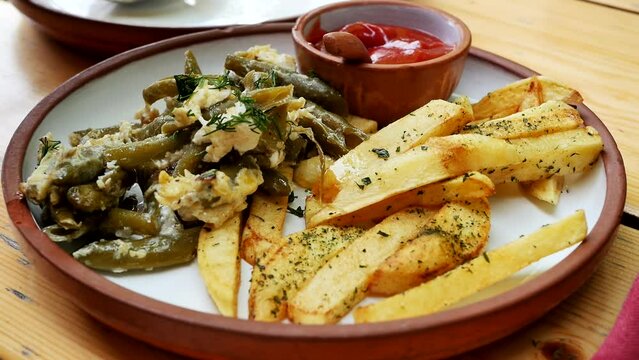 close-up spoon puts fried green beans with omelet in a plate with golden fried potatoes with spices and salt. Combo dish of fried potatoes and beans. With added ketchup