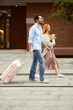 Beautiful Young Couple, Man And Woman Going On Summer Vacation Together With Dog. Man Pulling Suitcase. People Going Along Street. Concept Of Family, Relationship, Travelling, Vacation, Ad