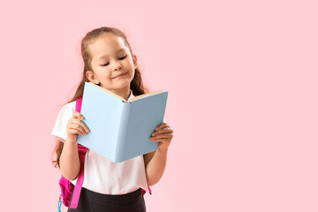 Little schoolgirl with book on pink background