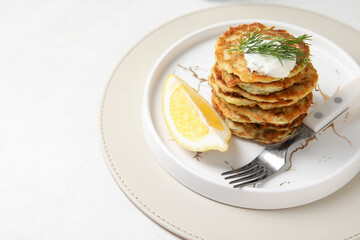 Plate of tasty zucchini fritters with sour cream on light background