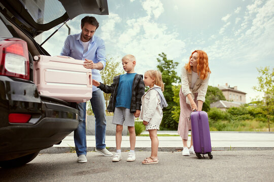 Man and woman, parents going on vacation with their children, packing suitcases into car. Car trip. Weekend adventures. Concept of family, childhood and parenthood, travelling, vacation, ad