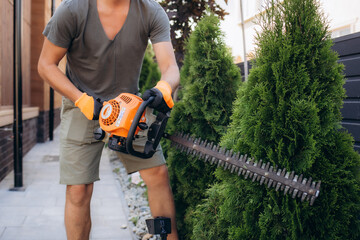 Man with garden gasoline scissors cutting a green bush Thuja - hedge crown formation. Work in the...