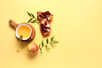 Wooden board with bowl of honey, pomegranate and apple for Rosh Hashanah celebration (Jewish New Year) on yellow background