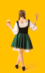 Beautiful Octoberfest waitress with beer and pretzel on yellow background, back view