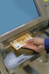 Detail of a man's hand taking euro bills out of an ATM.
