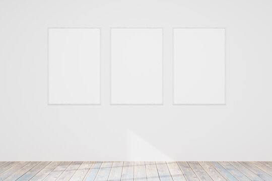 Three empty wooden photo or picture frames hang on a white wall. Wooden floor. Models of paintings, posters, photographs. Design template for layout. 3D rendering.
