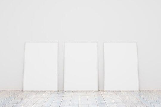 Three empty wooden frames for a photo or picture on the floor near a white wall. Models of paintings, posters, photographs. Design template for layout. 3D rendering.