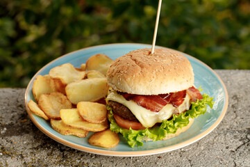 The yummy burger with homemade craft french fries on the blue plate filmed outside 