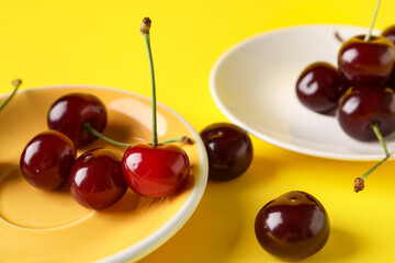 Plates with sweet cherries on yellow background