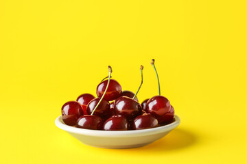 Plate with sweet cherries on yellow background