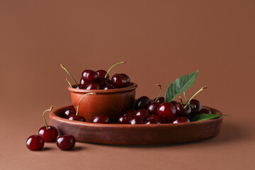 Bowl and plate with sweet cherries on brown background