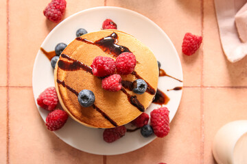 Plate of tasty pancakes with raspberries and blueberries on beige tile background