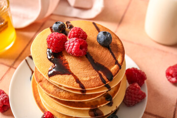 Plate of tasty pancakes with raspberries and blueberries on beige tile background