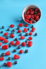 Cup with fresh raspberries and blueberries on blue background