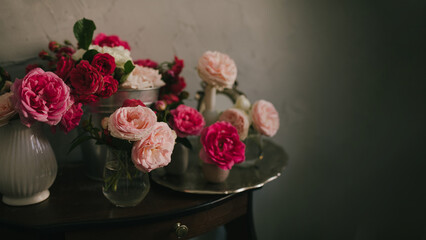 Still life with many different garden roses on a vintage table on grey background.