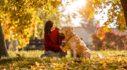 Beautiful girl with golden retriever dog sitting in autumn park with yellow leaves. Pretty young...