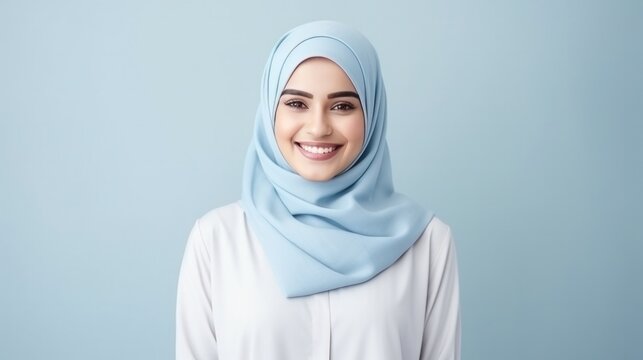 Smiling muslim beautiful woman with hijab and casual shirt standing over isolated light blue background.