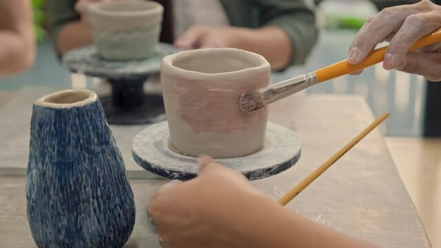 Close up of hand coloring clay pot with brush on pottery wheel