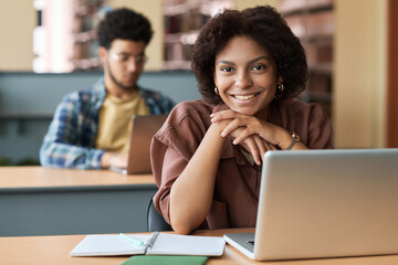 Portrait of African American student smiling at camera while sitting at desk with laptop in class