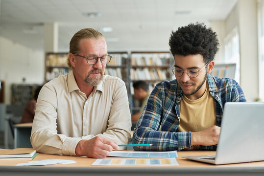 Teacher teaching migrant of new language while they sitting at desk with laptop and textbooks