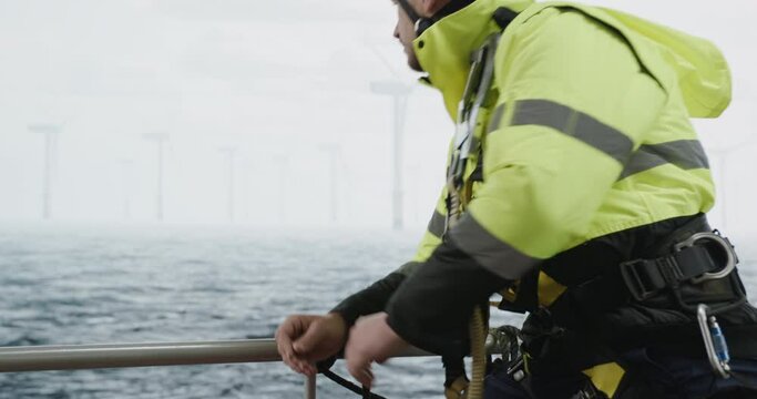 Maintenance engineer checking the data on tablet, approaching offshore wind turbine farm on a service vessel. Portrait of skilled professional preparing to work at high altitude