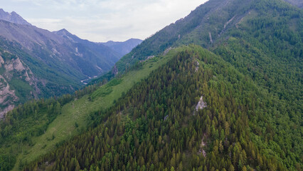 Aerial view of a high valley of the rocky mountain range, on which snow lies in places, near to the fast mountain river at summer cloud morning, orange color of the image