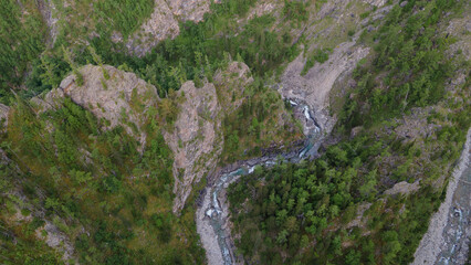 Aerial close view of the fast mountain river in valley of the rocky mountain ridges at summer cloud morning, green color of the image