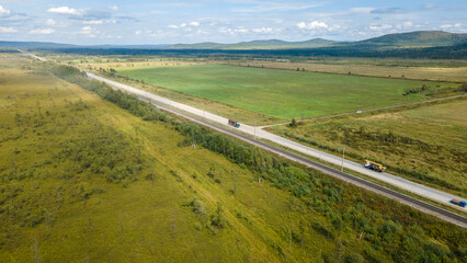 Aerial view of the country road and power lines near to the hill range, small coniferous forest and meadows agriculture at summer cloud sunny with horizon, shadows, color image, low height