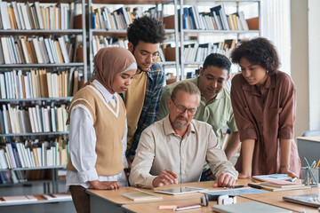 Group of students using tablet pc with teacher during lesson in the library
