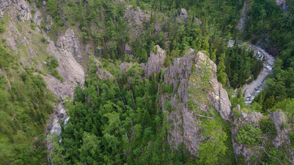 Aerial view of the mountain river in valley of the rocky mountain ridges, on which snow lies in places at summer cloud morning, orange color of the photo