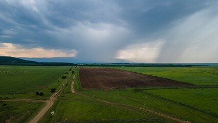 Naklejka premium Aerial view of the meadows with cows and horses near to the mountain ridge and country road at summer cloud rain day, blue color of the picture