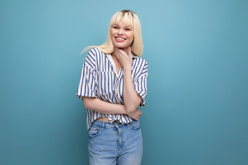 Cheerful cute blond 25 year old female person in a striped blouse and jeans on a blue background
