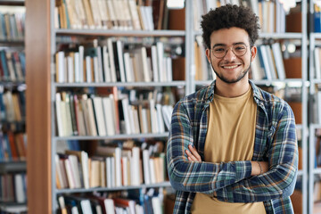 Portrait of adult student standing with his arms crossed and smiling at camera in library at college