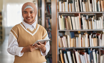 Portrait of muslim student smiling at camera while using tablet pc in library