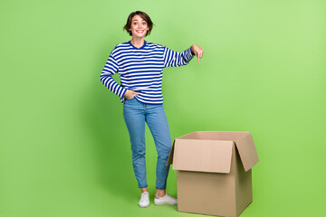 Full length photo of overjoyed woman wear sailor shirt denim trousers indicating at box hand in pocket isolated on green color background