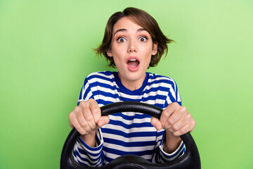 Photo of young funky girl open mouth hold steering wheel wear striped shirt unexpected oncoming way car isolated on green color background