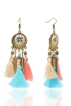 Subject shot of golden long graceful boho style earrings decorated with colored enamel, beads and colorful tassels made of cotton threads. The earrings are isolated on the white background.