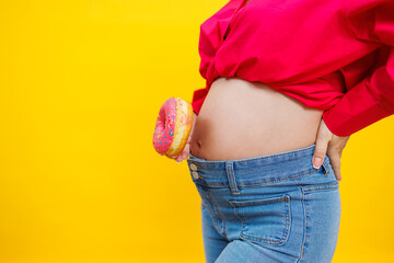 Pregnant young woman in a pink shirt with a donut in her hands. Junk food during pregnancy. Hungry...